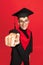 Studio shot of young smiling, cheerful student, graduate in mortarboard isolated over red studio background.