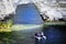 Studland, Dorset, UK - June 04 2018: Three men in a small rubber dinghy, about to go through a chalk cliff arch on the sea coastbl