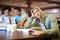 Studying bores him. A young student looking bored while in his classmates study int the background.