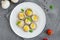 Stuffed mushrooms with quail eggs on a white plate with basil and thyme leaves on a dark concrete background. Easter appetizer.