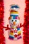 Stuffed snowman with a multicolored scarf and hat, with two buttons in the shape of a star and arms in the shape of a red branch