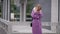 Stunning blonde woman in stylish purple outfit waiting outside in rainy weather, cold autumn.