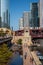 Stunning and colorful view of two el trains crossing the Chicago River and Wacker Dr. while commuters walk on riverwalk next to