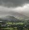 Stunning epic landscape image across Derwentwater valley with falling rain drifting across the mountains causing pokcets of light