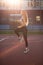 Stunning fitness girl in sport apparel warms up on a tennis court in soft evening sun light