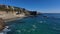 Stunning footage of the vast blue ocean water and the waves crashing into rocks at the beach with silky brown sand and rocks