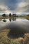 Stunning landscape image of dramatic storm clouds over Kelly Hall Tarn in Lake District during late Autumn Fall afternoon