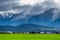 A stunning landscape scene of a rural area with green grassland cloudy snow mountain and sun rays after raining day. I