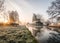 Stunning old canal house boats landscape sunrise in countryside with river and single lone wooden bench. Frost on grass.