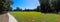 A stunning panoramic shot gorgeous summer landscape in the park with lush green trees, grass and plants with a still blue lake