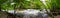 A stunning panoramic shot of the rushing river water of Big Creek river with lush green trees and large rocks on the banks