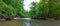 A stunning panoramic shot of the rushing river water of Big Creek river with lush green trees and large rocks on the banks