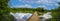 A stunning panoramic shot of the vast lake water with lush green trees and plants reflecting off the lake with blue sky and clouds