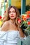 Stunning portrait with a beautiful brunette closing her eyes near blooming red flowers. White dress and red lipstick.