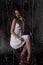 Stunning portrait of a sexy young brunette girl in a white dress sitting on a high chair on a black background. Low key. Beauty