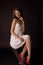 Stunning portrait of a sexy young brunette girl in a white dress sitting on a high chair on a black background. Low key. Beauty