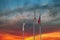 A stunning share of an American flag and two other flags flying on tall flag poles with blue sky and powerful red colored clouds