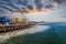 A stunning shot of a colorful Ferris wheel, rollercoaster and carnival games on a long brown wooden pier