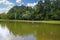 A stunning shot of a rippling green lake surrounded by lush green grass and lush green trees with people driving a golf cart