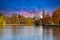 A stunning shot of the still blue waters of the lake in the park surrounded by gorgeous autumn colored trees