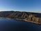 A stunning shot of the still lake waters and sand beach with majestic mountain ranges with blue sky