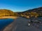 A stunning shot of the still lake waters and sand beach with majestic mountain ranges with blue sky