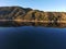 A stunning shot of the still lake waters and sand beach with majestic mountain ranges with blue sky