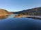 A stunning shot of the still lake waters and sand beach with majestic mountain ranges with blue sky