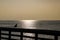 A stunning shot of the vast blue rippling ocean water at sunset with seagull standing on the rail of a brown wooden pier