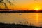 A stunning shot of a white motor boat sailing down the Mississippi river with a gorgeous yellow and red sunset with trees