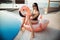 Stunning slim girl is wearing black bikini sitting in swimming pool with blue water on a pink flamingo mattress, summer