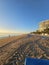 a stunning summer landscape along the beach at sunrise with blue and white lounge chairs, blue ocean water, palm trees, hotels