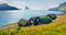 Stunning summer scene of Bour village with typical turf-top houses and Tindholmur cliffs on background. Panoramic morning view of