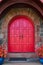 Stunning vibrant red arched double doors with stone arch and pair of red plants in blue pots