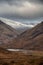 Stunning Winter landscape image of snowcapped Three Sisters mountain range in Glencoe Scottish Highands with dramatic sky