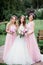 Stunning young bride and bridesmaids in pink dresses stand with wedding bouquets in the park