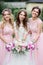 Stunning young bride and bridesmaids in pink dresses stand with wedding bouquets in the park