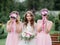 Stunning young bride and bridesmaids in pink dresses stand with wedding bouquets in the park