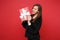 Stunning young woman in fur sweater hold red striped present box with gift ribbon isolated on red background. Valentine