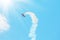 Stunt plane trailing smoke bright sun and clouds