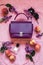 Styled violet lifestyle fashion leather bag surrounded by lilacs flowers and greenery on minimal peach  background setup