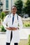 Stylish african american doctor with stethoscope and lab coat posed at backyard of hospital