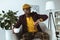 stylish african american man with cup of coffee looking at watch and sitting in armchair