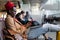 Stylish African American traveler millennial man resting and sitting in hall of airport, using phone, works remotely on laptop