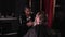 A stylish African-American woman in a black raincoat in a barber shop braids her braids into a beard for a male client.