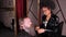 A stylish African-American woman in a black raincoat in a barber shop braids her braids into a beard for a male client.