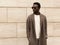 Stylish african man model looking away wearing brown knitted cardigan, sunglasses on city street over brick wall