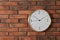 Stylish analog clock hanging on brick wall.