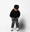 Stylish asian boy in black hoodie, jeans and white sneakers stands on a white background.