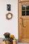 Stylish autumn decor of farmhouse entrance or porch. Autumn rustic wreath, pumpkins and flower pots at front door. Fall